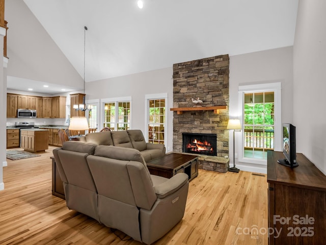 living area with high vaulted ceiling, light wood finished floors, a fireplace, and healthy amount of natural light