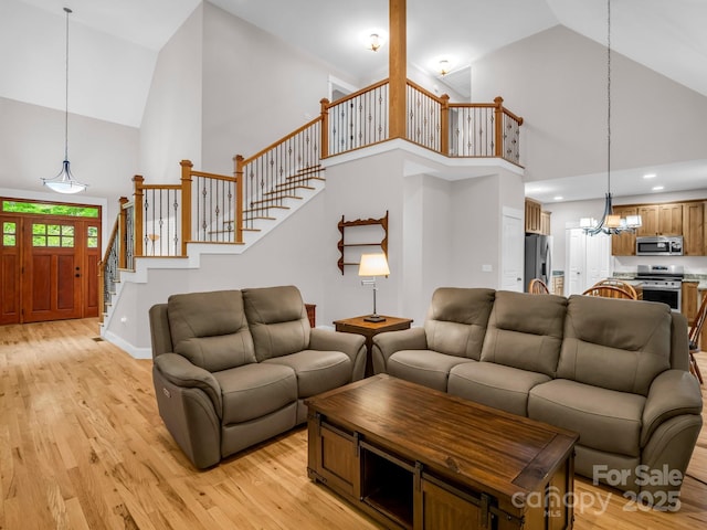 living room with high vaulted ceiling, a chandelier, stairs, light wood-type flooring, and baseboards