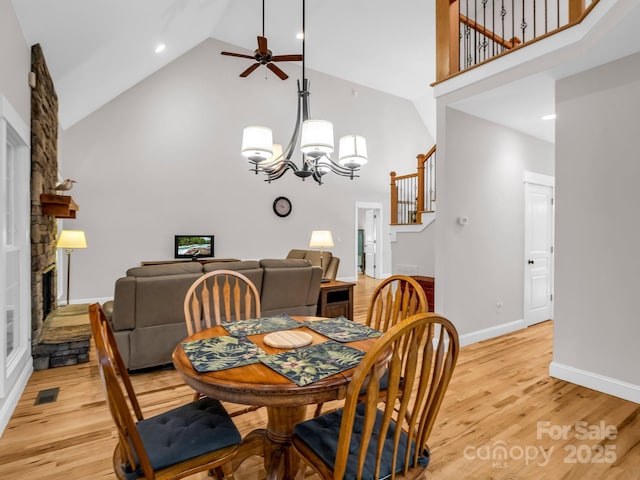 dining area with high vaulted ceiling, a fireplace, a ceiling fan, light wood-type flooring, and a chandelier