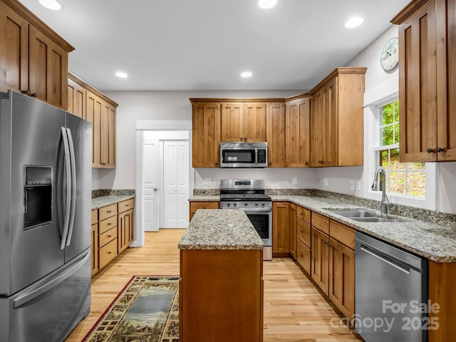 kitchen with stainless steel appliances, a sink, a kitchen island, light wood-style floors, and light stone counters