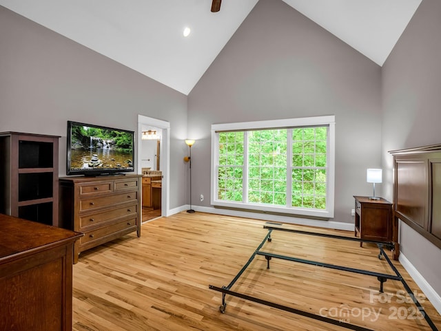bedroom featuring high vaulted ceiling, light wood-style floors, baseboards, and ensuite bath