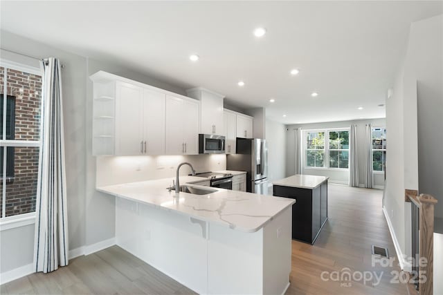 kitchen featuring appliances with stainless steel finishes, a sink, a center island, open shelves, and light wood finished floors
