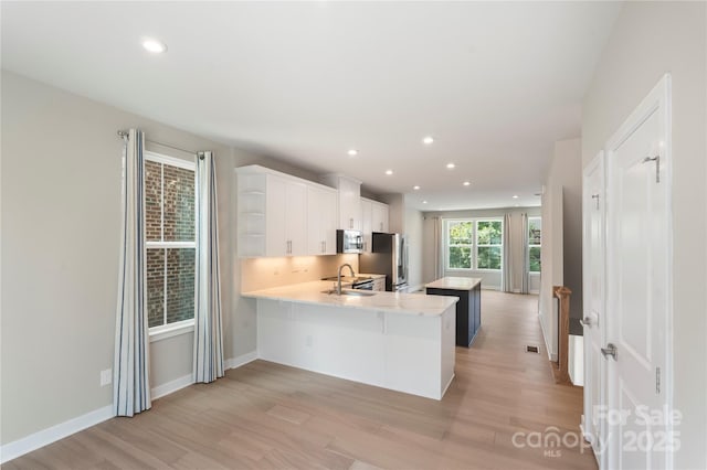 kitchen with appliances with stainless steel finishes, a sink, light countertops, light wood-style floors, and a peninsula