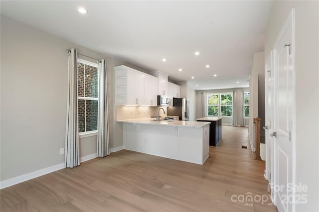 kitchen with stainless steel fridge, a sink, light countertops, a peninsula, and light wood-style flooring