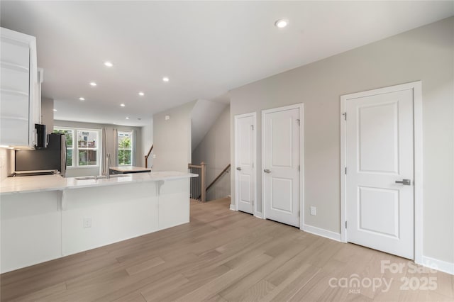 kitchen with a sink, a peninsula, light wood finished floors, recessed lighting, and white cabinets