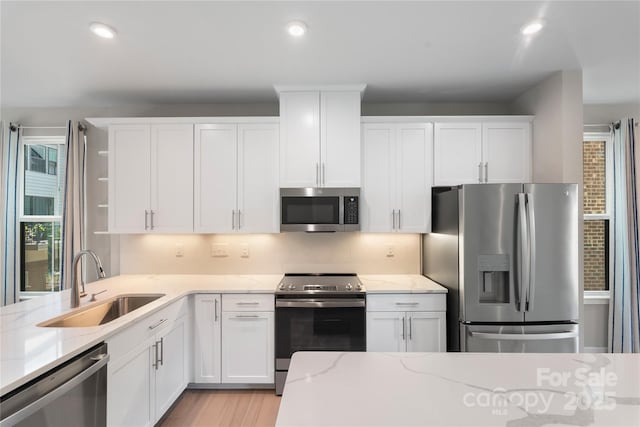 kitchen with appliances with stainless steel finishes, a sink, white cabinetry, light stone counters, and recessed lighting