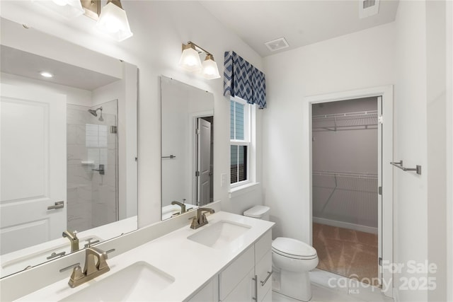 bathroom featuring tiled shower, a spacious closet, toilet, and double vanity