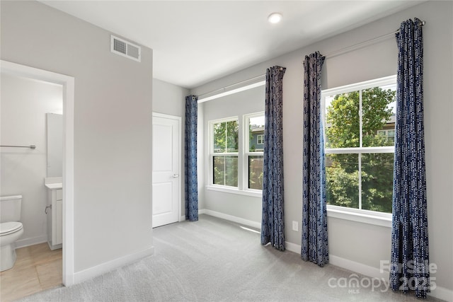 unfurnished bedroom with multiple windows, baseboards, ensuite bathroom, and carpet floors