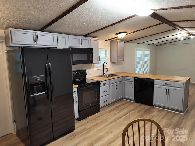 kitchen featuring black appliances, a sink, gray cabinets, butcher block counters, and a peninsula