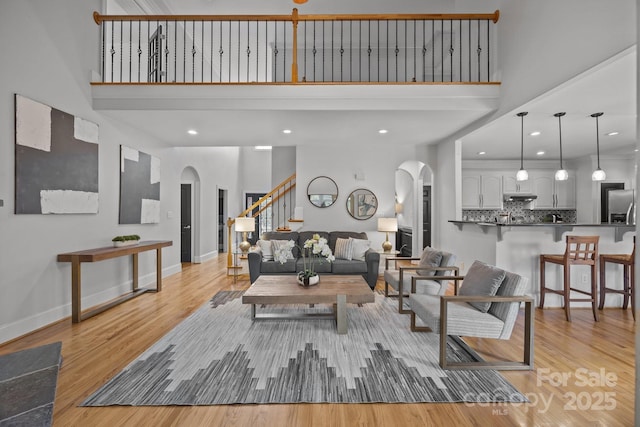 389 Ponderosa Cir, Mooresville, NC 28117 - living area featuring arched walkways, a towering ceiling, stairway, light wood-style flooring, and baseboards