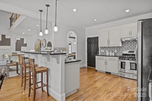 389 Ponderosa Cir, Mooresville, NC 28117 - kitchen with stainless steel appliances, arched walkways, under cabinet range hood, dark countertops, and crown molding