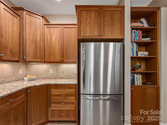 4 Alsatian Ln, Asheville, NC 28805 - kitchen featuring freestanding refrigerator, light stone countertops, decorative backsplash, and brown cabinetry