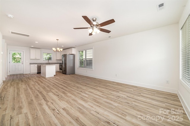 unfurnished living room featuring a chandelier, light wood-style flooring, baseboards, and plenty of natural light