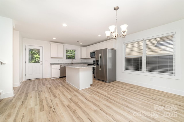 kitchen featuring appliances with stainless steel finishes, a kitchen island, white cabinetry, light wood-style flooring, and a chandelier