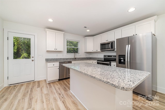 kitchen with stainless steel appliances, light wood-style floors, white cabinets, a kitchen island, and a sink