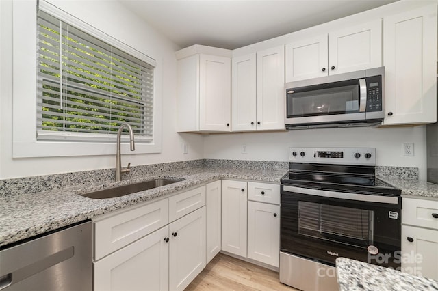kitchen featuring stainless steel appliances, a sink, white cabinetry, light wood-style flooring, and light stone counters