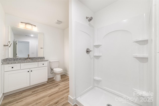 bathroom with toilet, wood finished floors, a shower, vanity, and baseboards