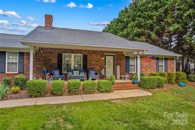 view of front of house featuring a front yard, a chimney, brick siding, covered porch, and a shingled roof