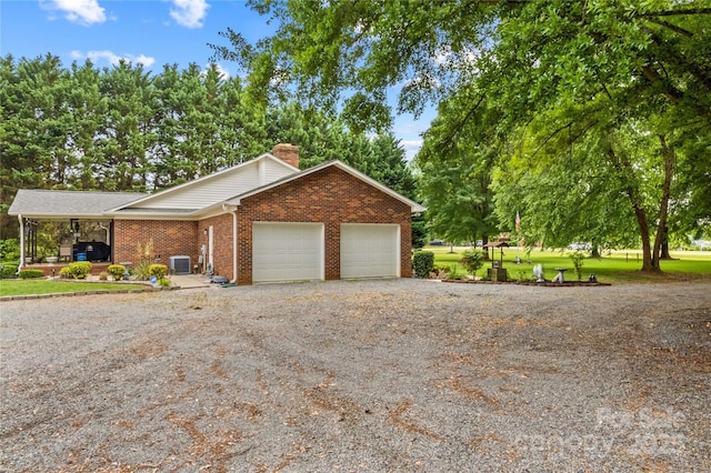 view of front of home with dirt driveway, brick siding, a chimney, a garage, and central AC unit