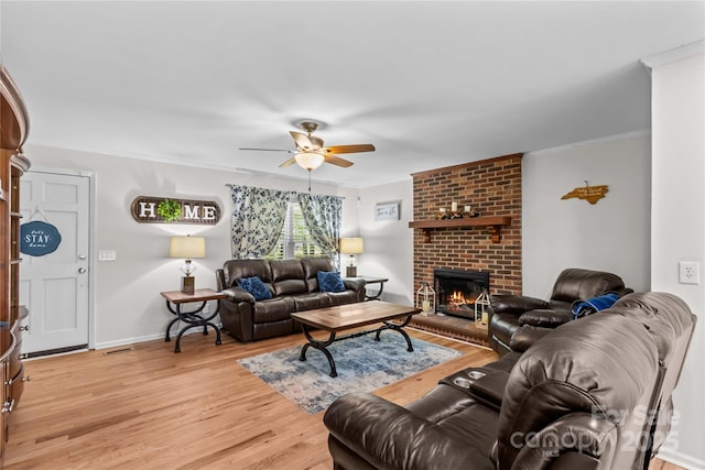living room with ceiling fan, a brick fireplace, light wood-type flooring, ornamental molding, and baseboards