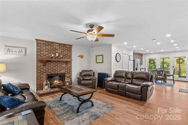 living area with a ceiling fan, light wood-style flooring, a brick fireplace, ornamental molding, and recessed lighting
