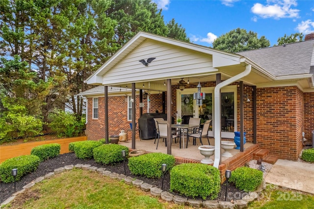 rear view of house with brick siding, roof with shingles, and a patio