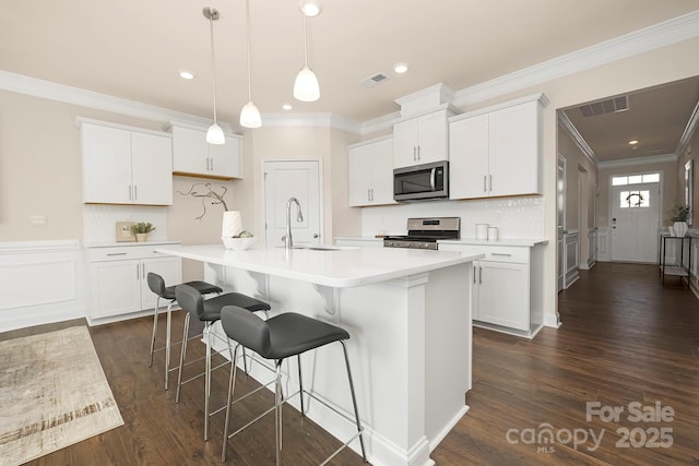 kitchen featuring stainless steel appliances, a sink, crown molding, light countertops, and a kitchen bar