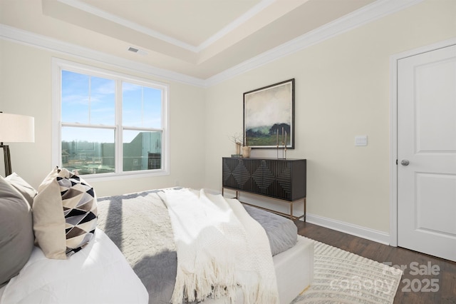 bedroom with a tray ceiling, wood finished floors, crown molding, and baseboards