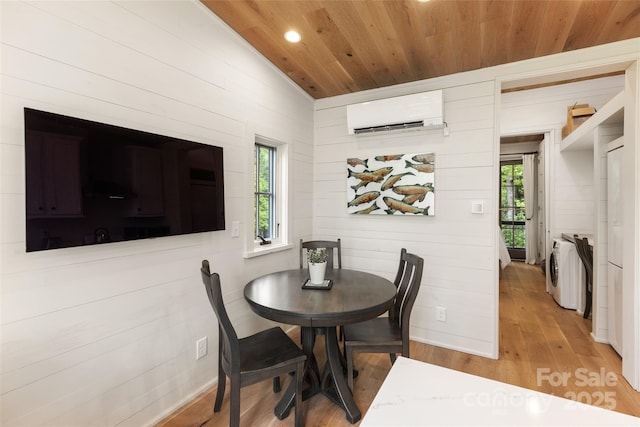 dining room featuring an AC wall unit, wood ceiling, wooden walls, washing machine and clothes dryer, and healthy amount of natural light