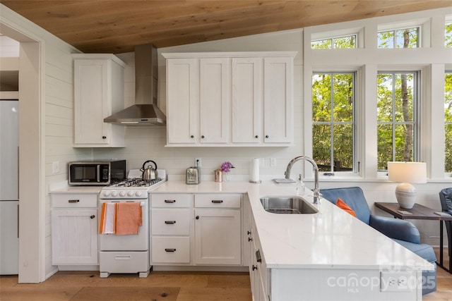 kitchen featuring wall chimney exhaust hood, a sink, white range with gas cooktop, stainless steel microwave, and vaulted ceiling