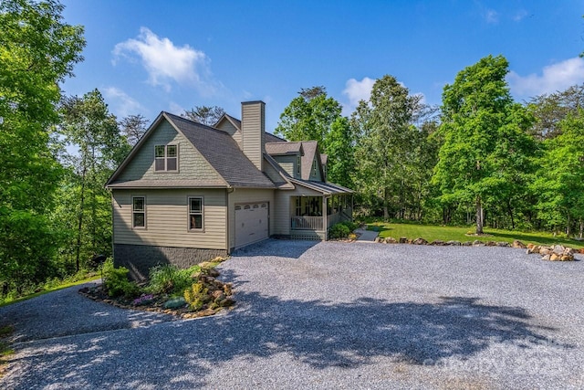view of side of home with gravel driveway, an attached garage, a porch, a chimney, and a shingled roof