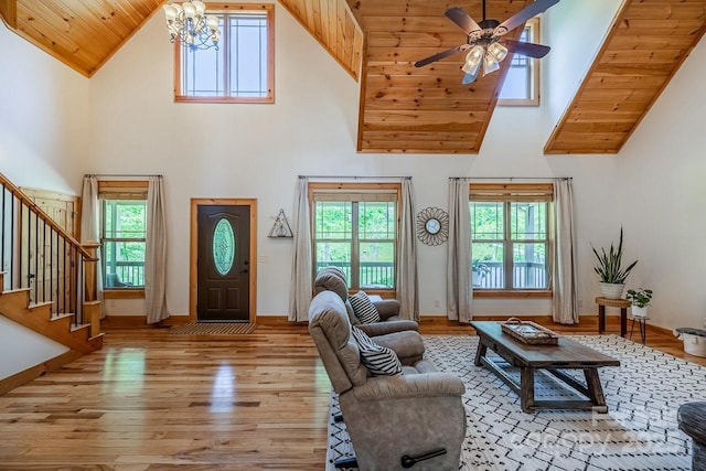 living area featuring high vaulted ceiling, hardwood / wood-style flooring, a chandelier, stairs, and a ceiling fan