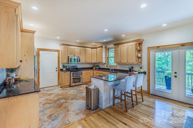 kitchen featuring stainless steel appliances, light brown cabinets, a sink, backsplash, and a breakfast bar