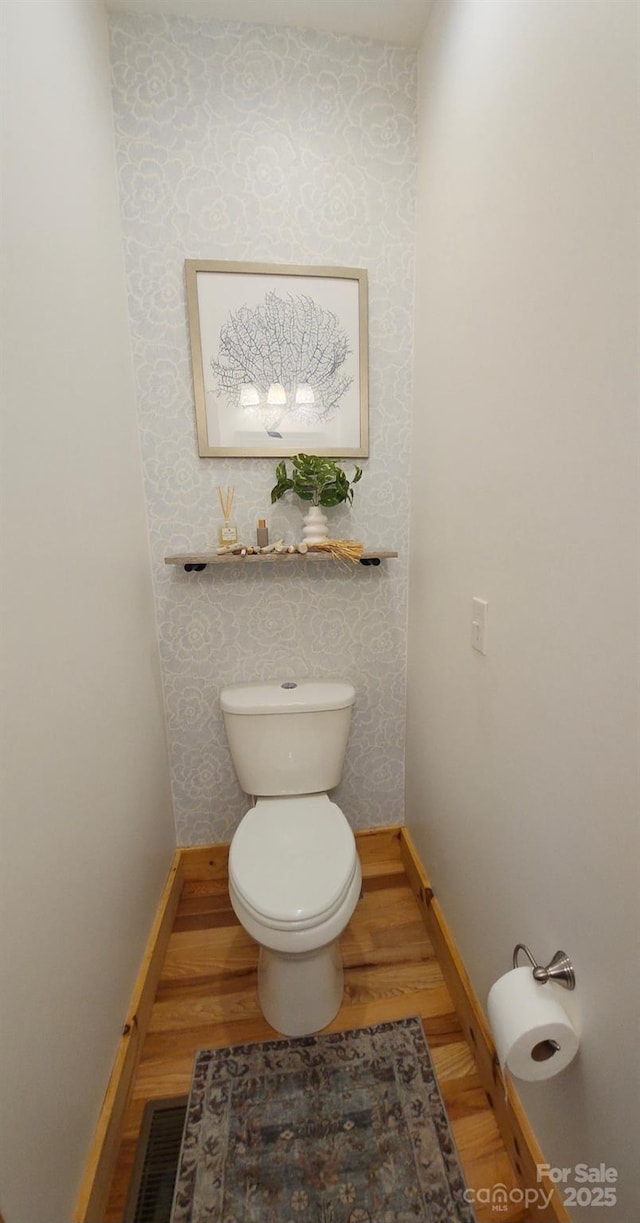 bathroom featuring wallpapered walls, baseboards, wood finished floors, and toilet