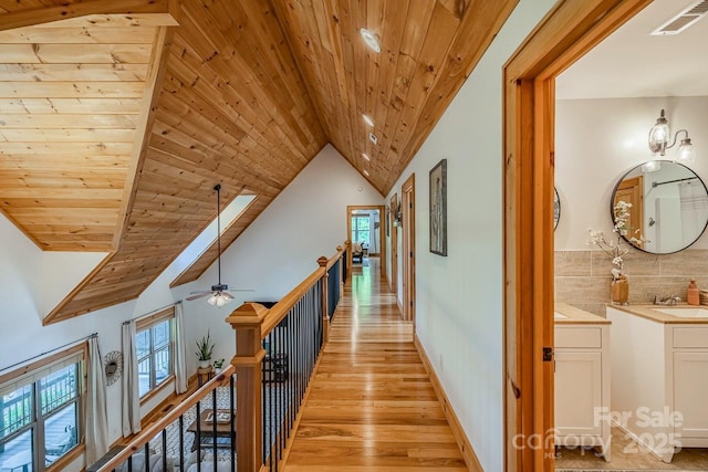 corridor featuring an upstairs landing, wood ceiling, a sink, light wood-style floors, and baseboards