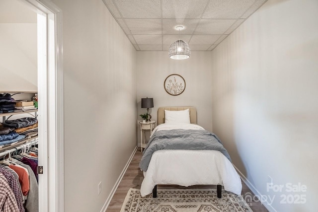 bedroom with wood finished floors, a paneled ceiling, and baseboards