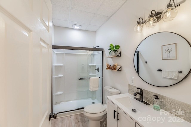 full bathroom with toilet, a paneled ceiling, a shower stall, wood finished floors, and vanity