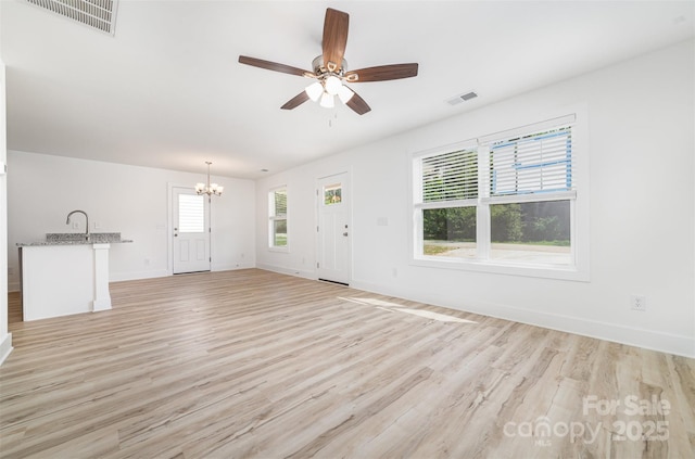 unfurnished living room with a chandelier, ceiling fan, light wood-type flooring, baseboards, and a sink