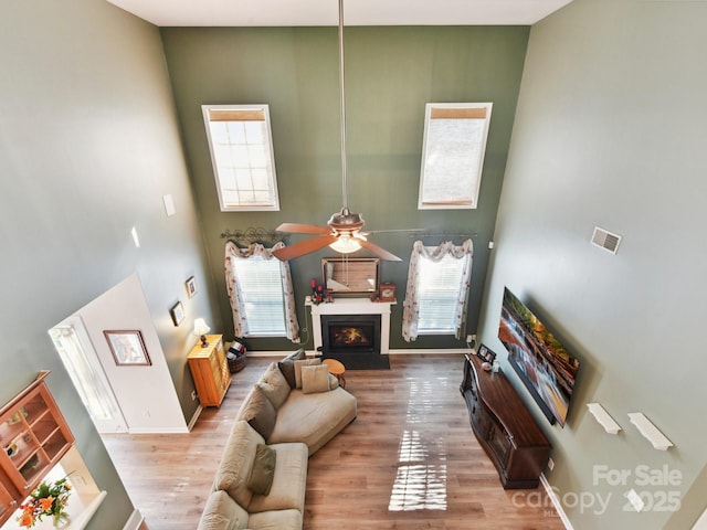 1564 Trippett St NW, Concord, NC 28027 - living area featuring wood finished floors, a ceiling fan, a towering ceiling, baseboards, and a warm lit fireplace