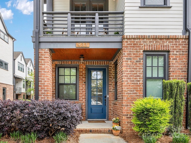 view of exterior entry featuring a balcony and brick siding