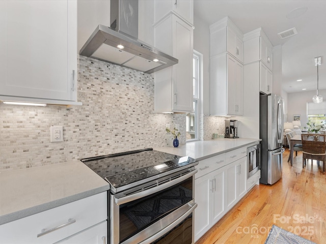 kitchen featuring stainless steel appliances, wall chimney exhaust hood, white cabinetry, light countertops, and recessed lighting