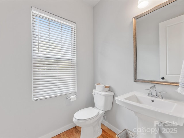 half bathroom with baseboards, toilet, wood finished floors, and a sink