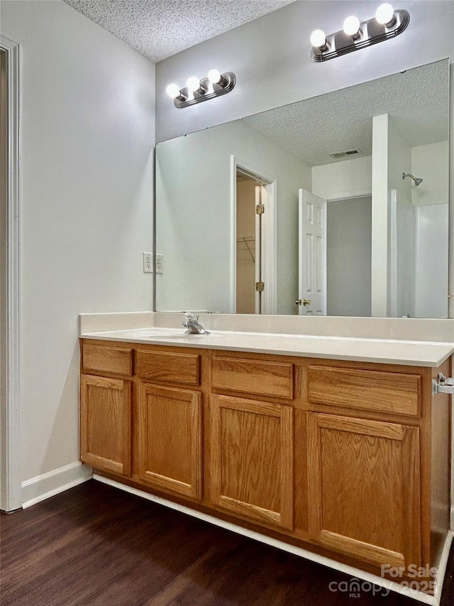 710 Woodington Ln, Charlotte, NC 28214 - bathroom featuring a textured ceiling, wood finished floors, vanity, baseboards, and a shower