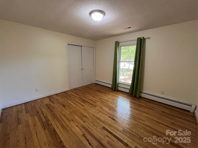 511 Evelyn Ave, Kannapolis, NC 28083 - unfurnished bedroom featuring wood finished floors, a textured ceiling, a closet, and a baseboard heating unit