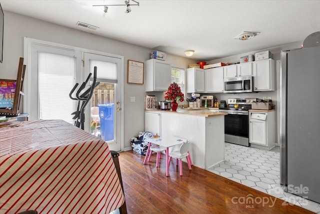 kitchen featuring stainless steel appliances, white cabinets, light countertops, and light wood finished floors