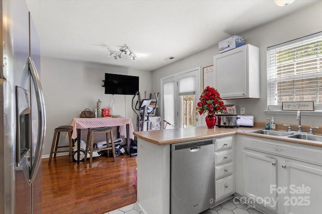 kitchen featuring appliances with stainless steel finishes, a sink, white cabinetry, a peninsula, and light countertops