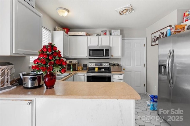 kitchen featuring appliances with stainless steel finishes, light countertops, white cabinets, a peninsula, and light tile patterned floors