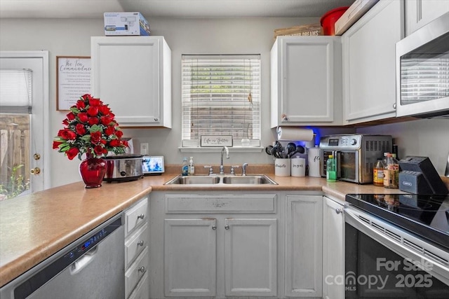 kitchen featuring appliances with stainless steel finishes, a sink, light countertops, and white cabinets