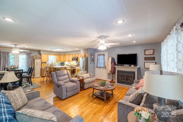 living area featuring a ceiling fan, recessed lighting, light wood-type flooring, and a glass covered fireplace