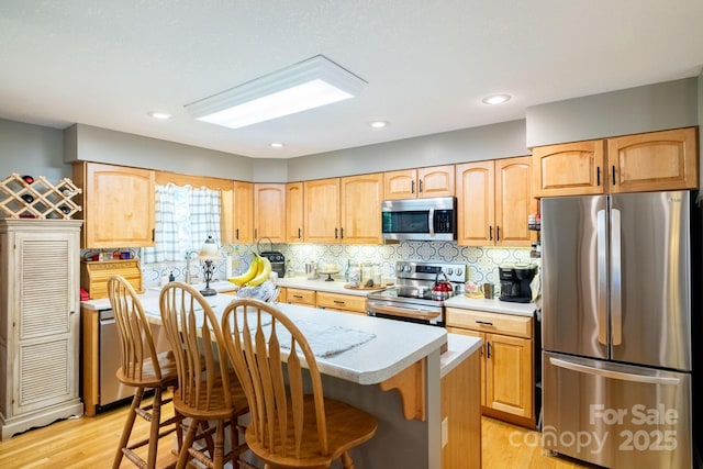 kitchen featuring appliances with stainless steel finishes, light countertops, light wood-type flooring, a center island, and decorative backsplash